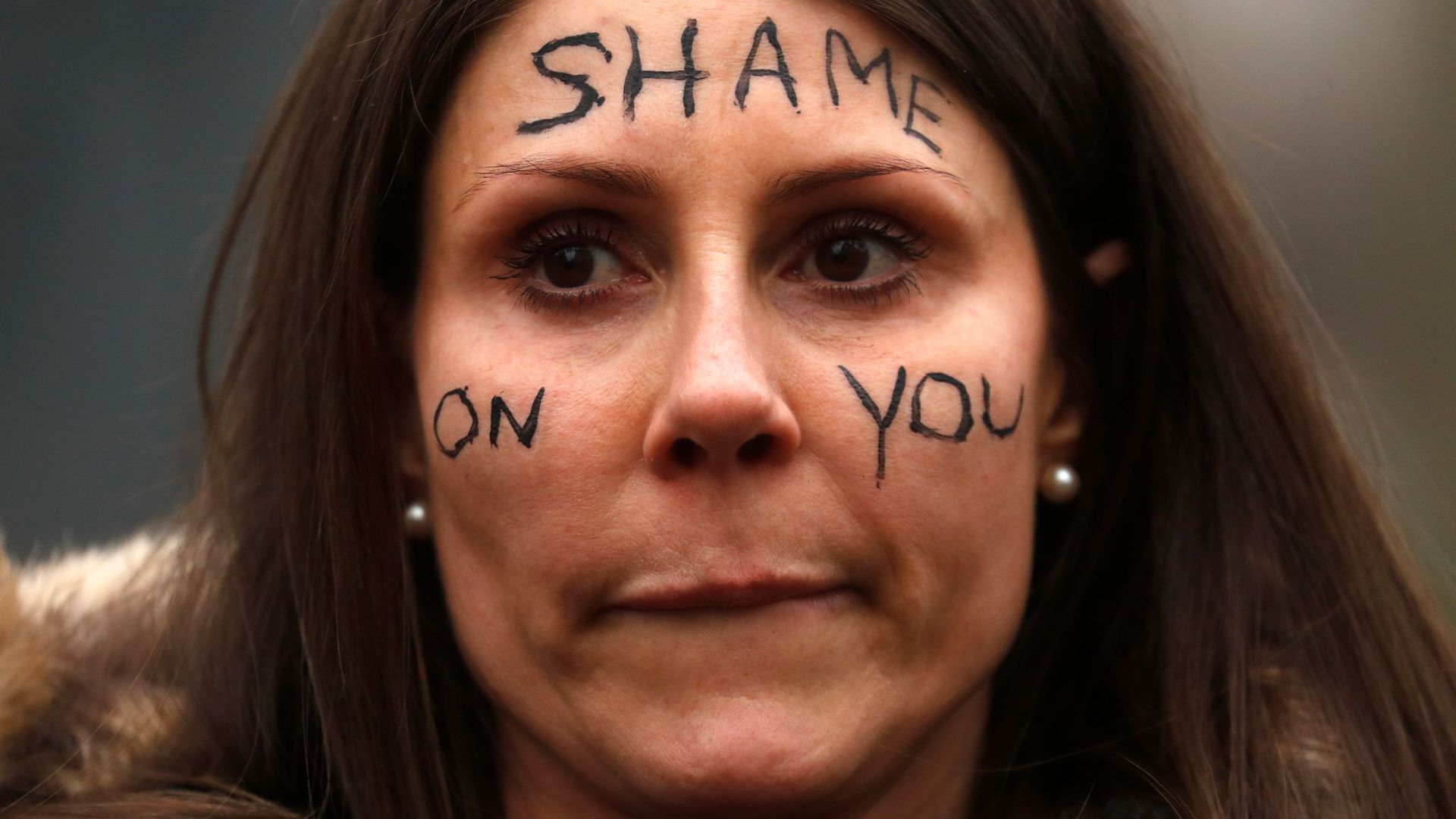 Eine Frau nimmt an einer Demonstration vor dem New Scotland Yard in London teil und trägt den Schriftzug „Shame On You“ auf ihrem Gesicht.