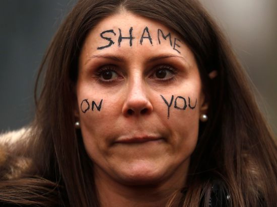 Eine Frau nimmt an einer Demonstration vor dem New Scotland Yard in London teil und trägt den Schriftzug „Shame On You“ auf ihrem Gesicht.