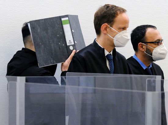 Der Angeklagte verbirgt im Sitzungssaal des Landgerichts Ingolstadt sein Gesicht hinter einem Aktenordner. Davor stehen seine Verteidiger.
