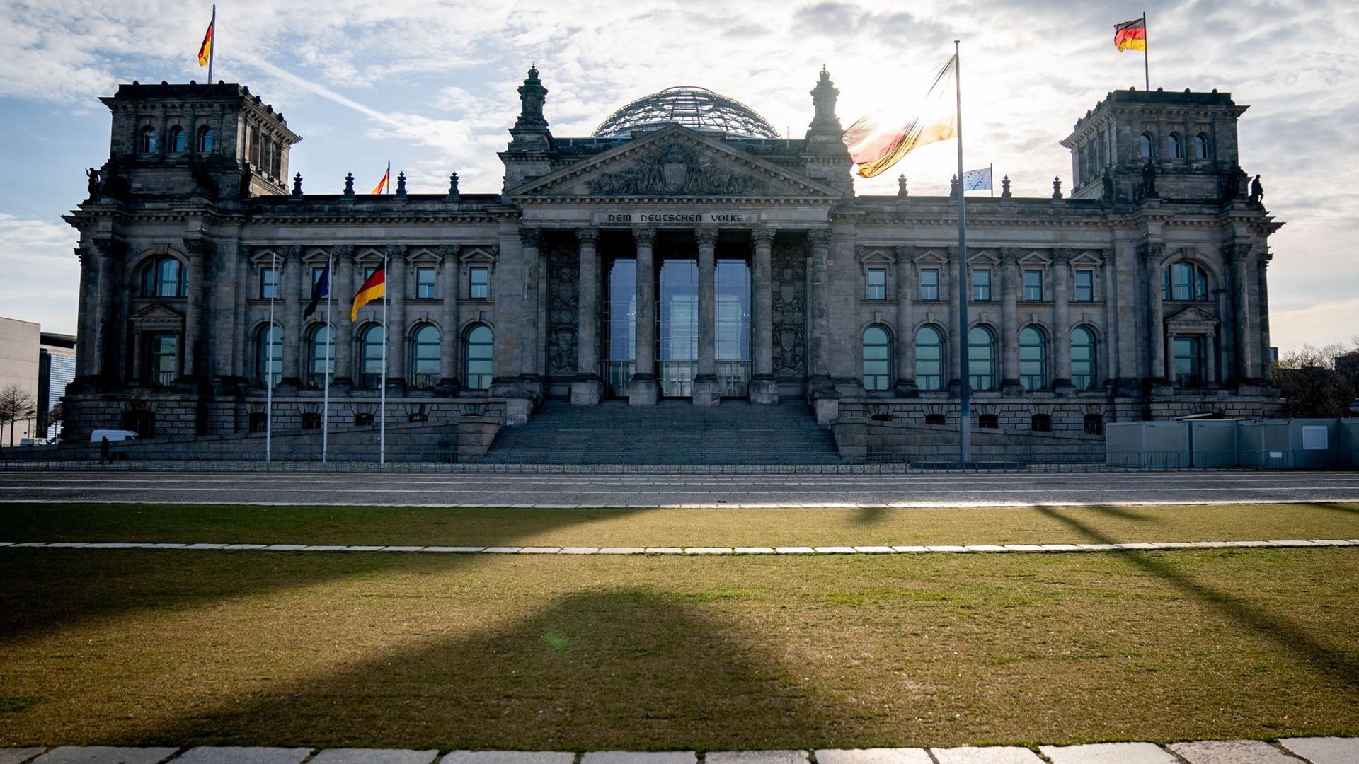 Die Sonne steht am Morgen hinter dem Reichstagsgebäude mit dem Bundestag.