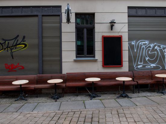 Leere Tische und Bänke stehen vor einer Kneipe in der Altstadt von Halle/Saale. Die Politik ringt um eine bundesweite Corona-Notbremse.
