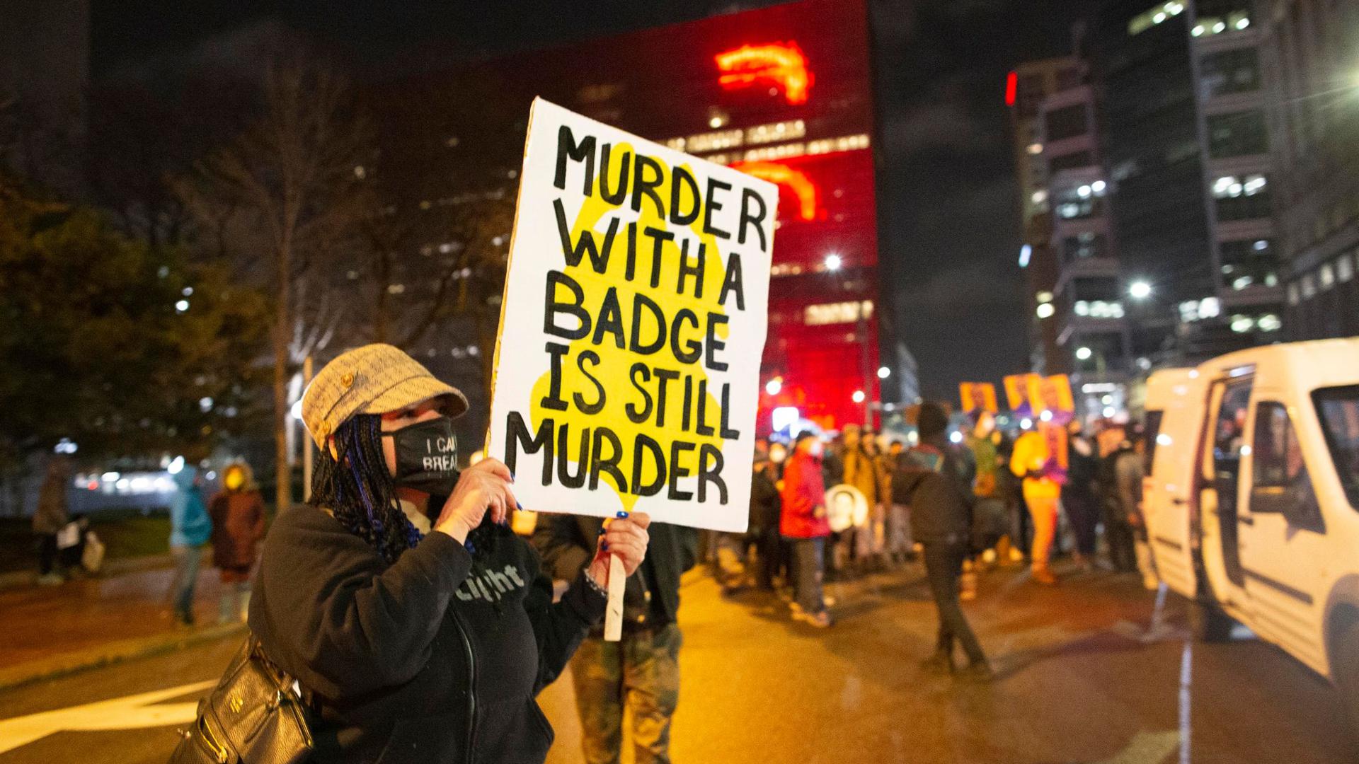Eine Frau hält während eines Protests in Minneapolis ein Schild mit der Aufschrift „Murder with a badge is still murder“ („Mord mit einer Dienstmarke ist immer noch Mord“).