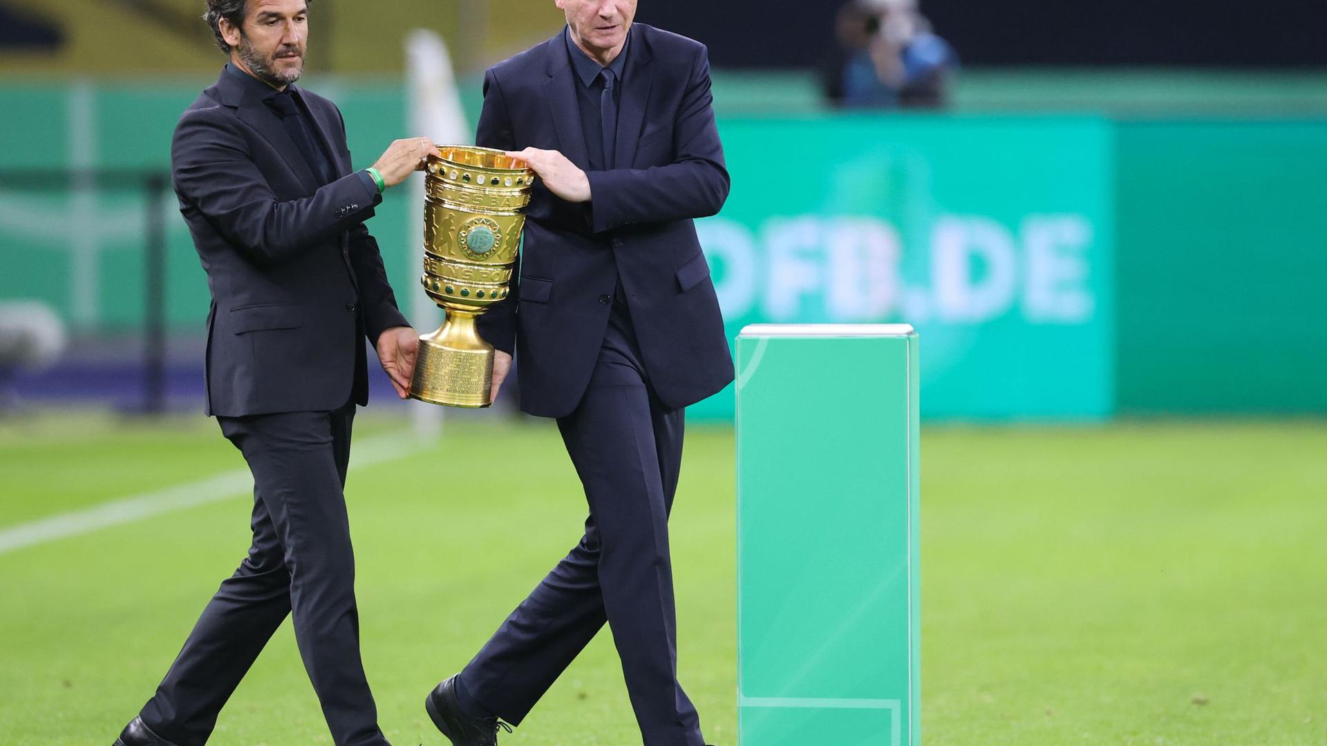 Karl-Heinz Riedle (l) und Perry Bräutigam tragen den DFB-Pokal auf das Feld.