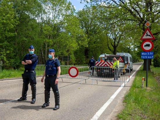 Belgische Polizisten sperren eine Straße in einem Waldstück ab.