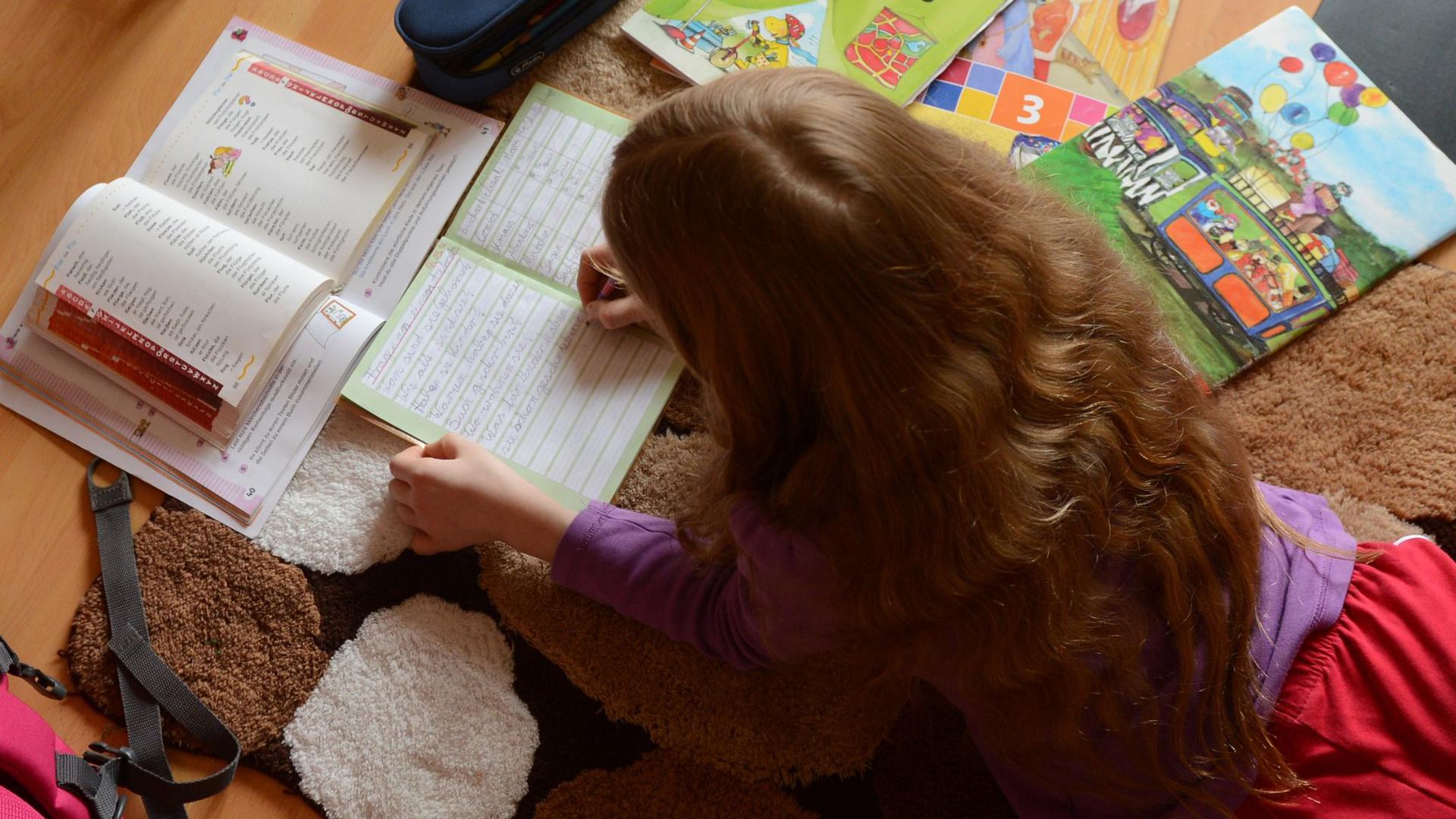 Ein Mädchen liegt auf einem Teppich in seinem Kinderzimmer und erledigt seine Hausaufgaben im Fach Deutsch.