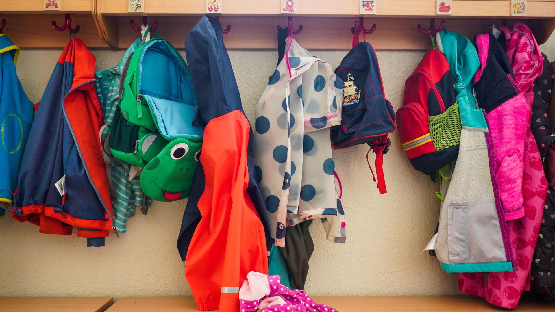 Jacken und Rucksäcke hängen an der Garderobe einer Kita. (Symbolbild)