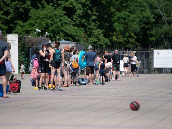 Menschen stehen bei warmem Wetter in einer Schlange vor dem Eingang zum Olympiabad in Berlin.