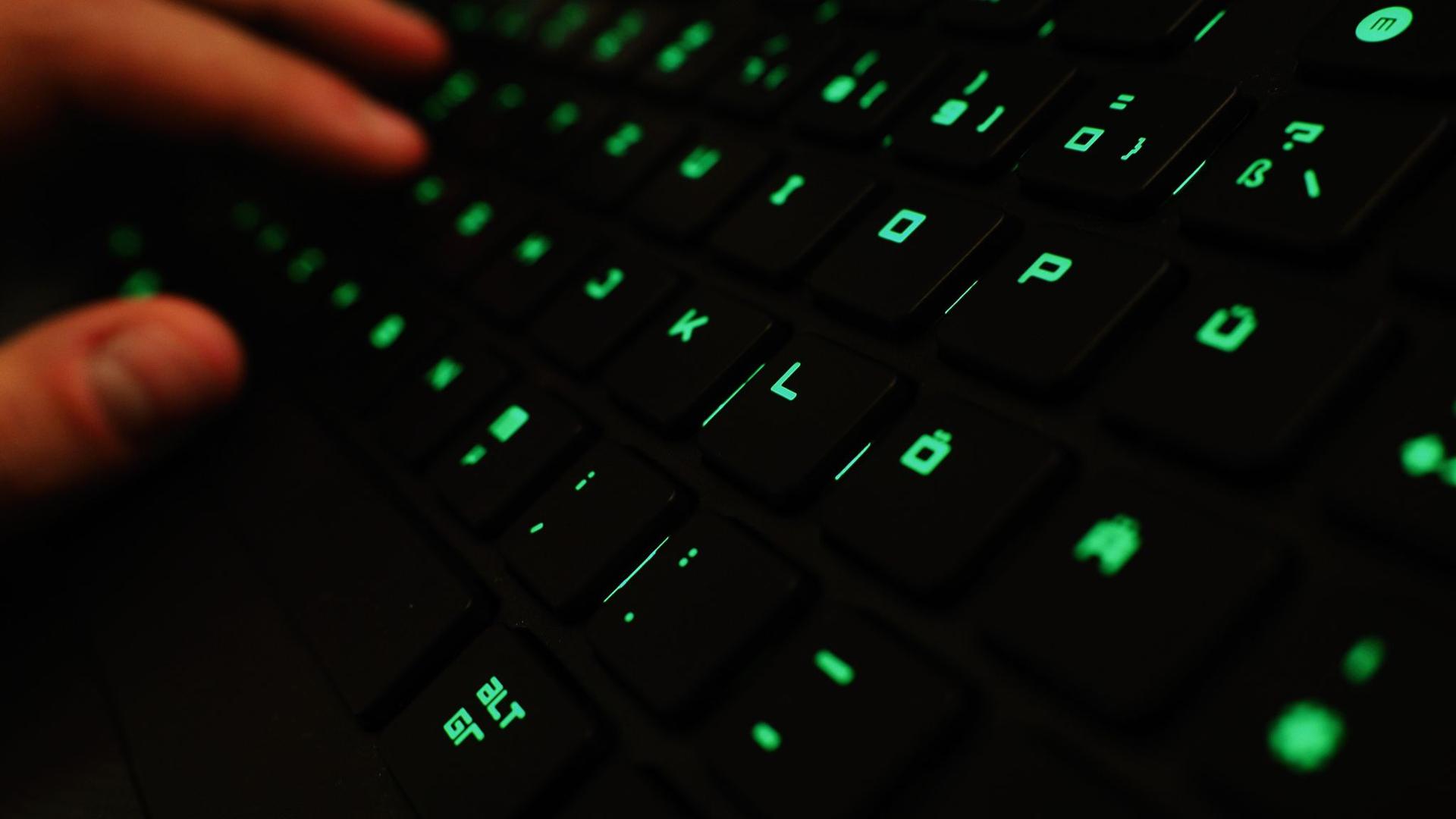 Ein Mann tippt auf einer beleuchteten Tastatur an einem Laptop.