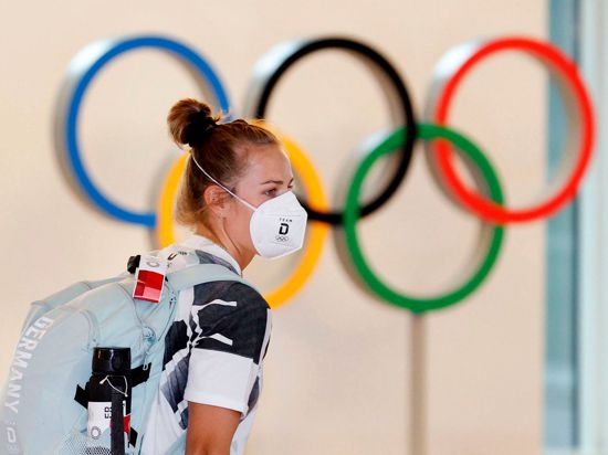 Eine deutsche Athletin trägt eine Schutzmaske und geht bei ihrer Ankunft am Flughafen Haneda an den Olympischen Ringen vorbei.