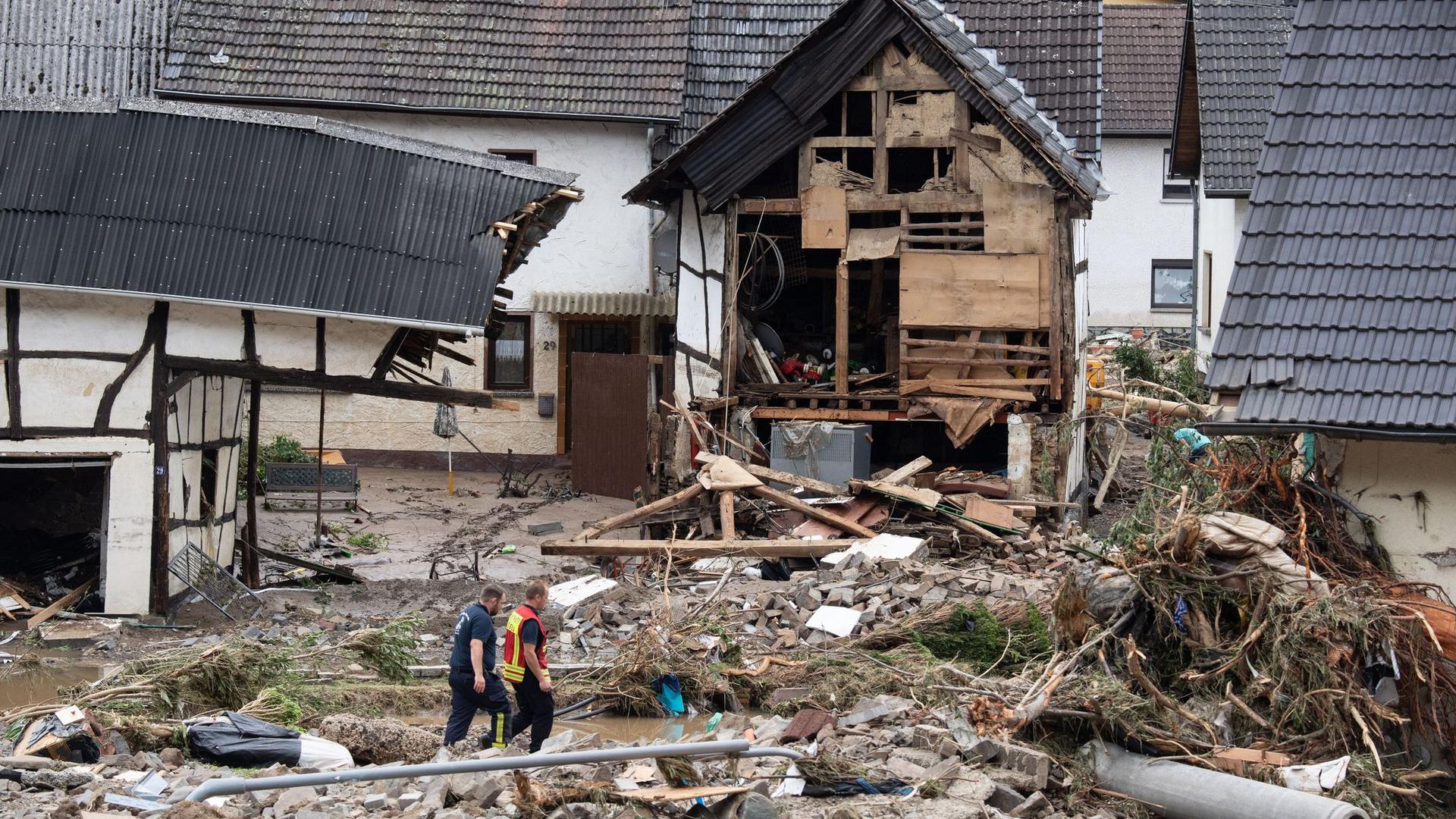 Zwei Feuerwehrleute gehen in dem Dorf im Kreis Ahrweiler nach dem Unwetter mit Hochwasser durch den Schutt. Mindestens sechs Häuser wurden durch die Fluten zerstört.