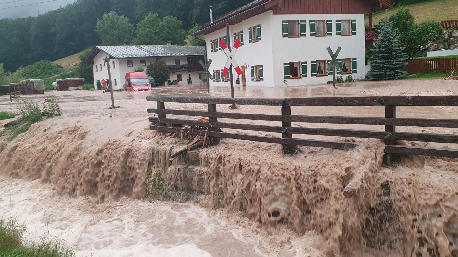 Wasser fließt über einen Platz vor einem Haus. Der Landkreis Berchtesgadener Land hat nach starkem Regen wegen Hochwassers den Katastrophenfall ausgerufen.