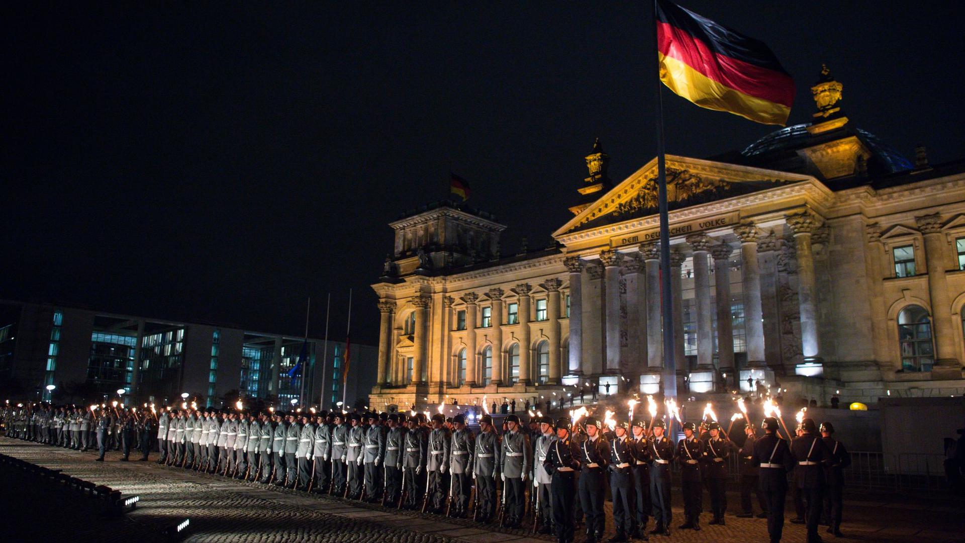 Zahlreiche Soldaten stehen bei einem Großen Zapfenstreich vor dem Reichstagsgebäude in Berlin.