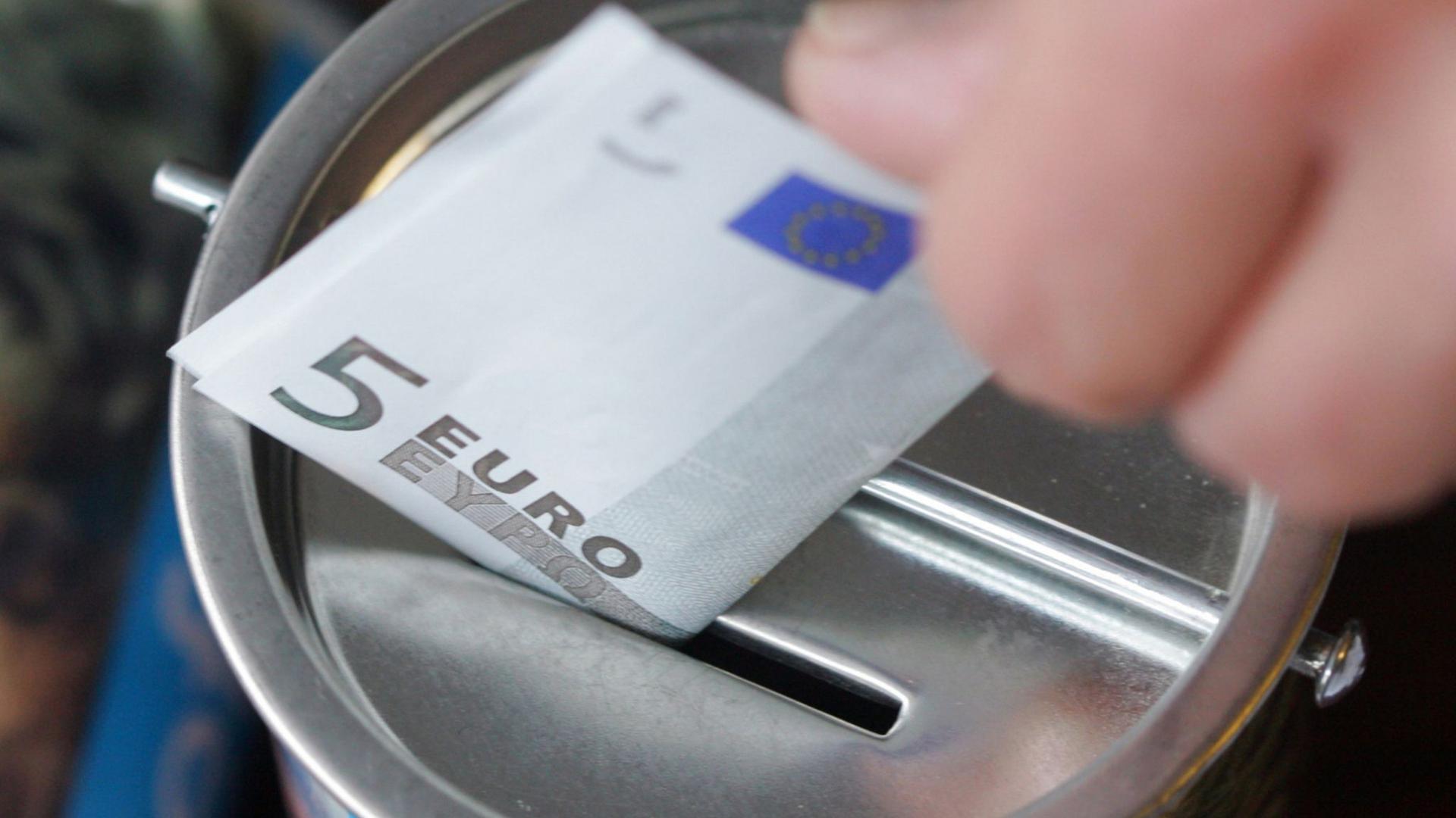 Ein Fünf-Euro-Schein wird in eine Spendendose gesteckt. Symbolbild