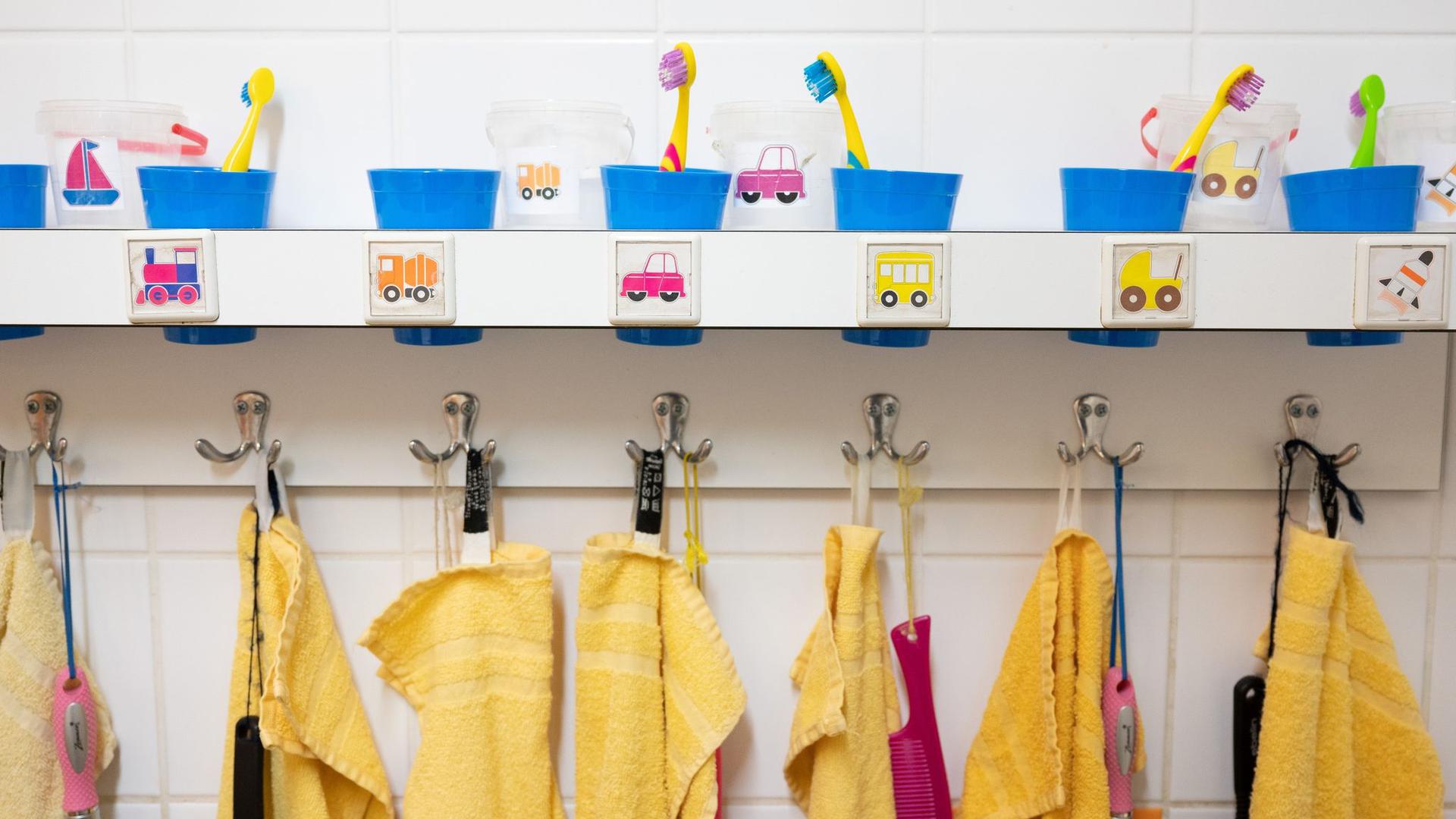 Handtücher und Zahnputzbecher hängen und stehen in einer Kindertagesstätte im Waschraum.