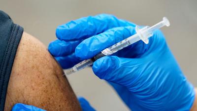 Eine Spitze mit einem Covid-Impfstoff wird in einen Arm gesetzt.