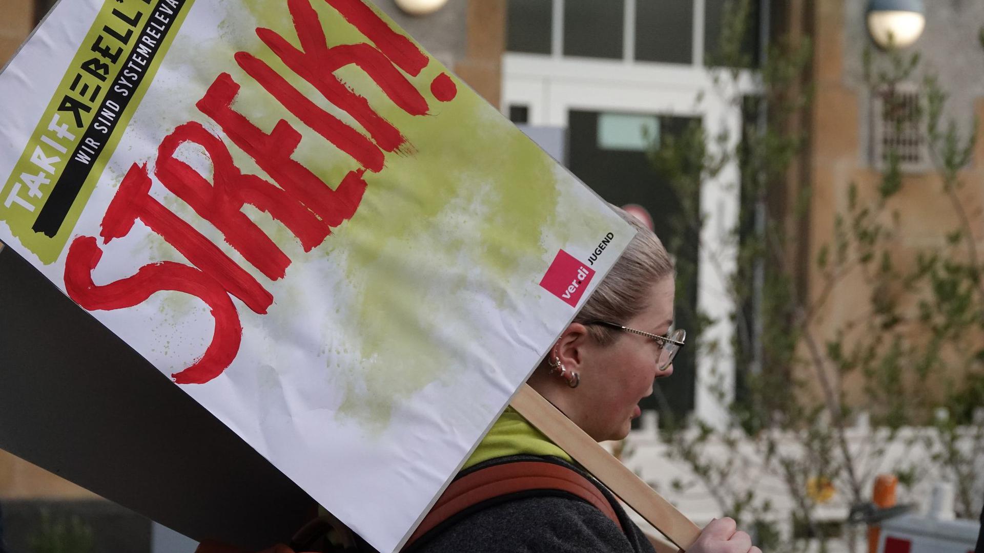 Eine Frau hält ein Schild hoch auf dem „Streik!“ steht.