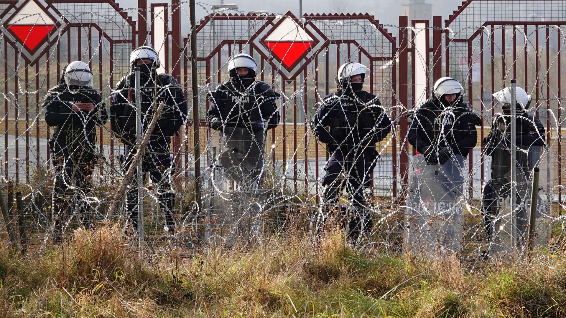 Polnische Sicherheitskräfte stehen an der Grenze hinter Stacheldraht.