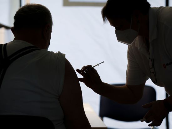 Eine Mitarbeiterin der Malteser impft einen Bürger in einem Impfzentrum in Sachsen-Anhalt.  Experten halten die vom designierten Bundeskanzler Olaf Scholz (SPD) angepeilten 30 Millionen zusätzlichen Impfungen bis Weihnachten für sehr ehrgeizig.