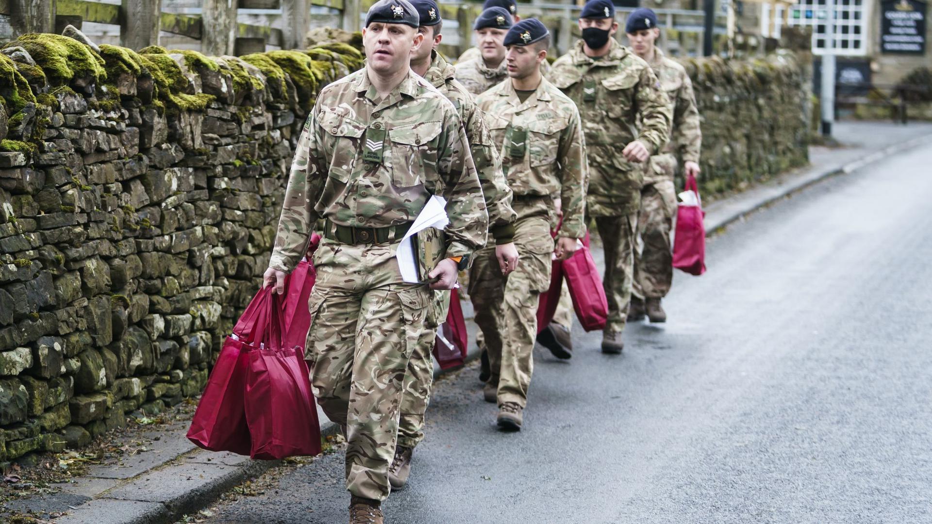 Angehörige der Streitkräfte tragen Versorgungspakete, um sie an Betroffene  im britischen St. John's Chapel zu verteilen.