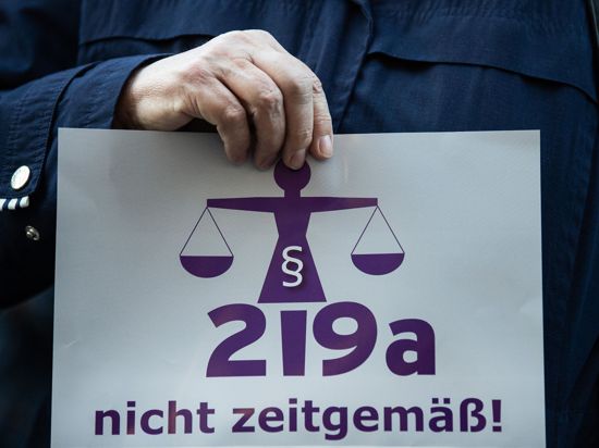 Eine Frau hält bei einer Kundgebung einen Zettel mit der Aufschrift „219a nicht zeitgemäß!“.