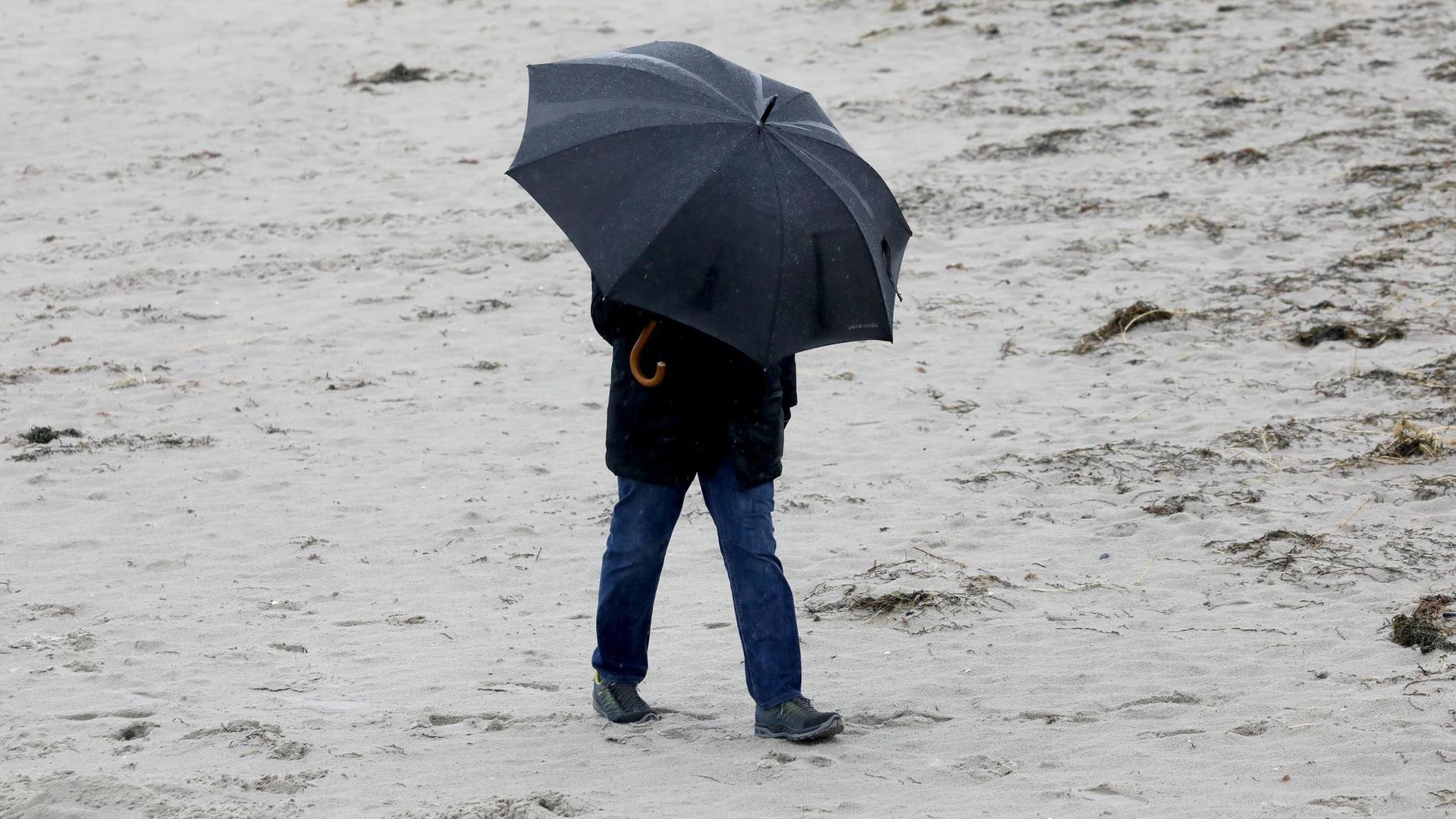 Spaziergänger mit wetterfester Kleidung und Regenschirm am Ostseestrand.
