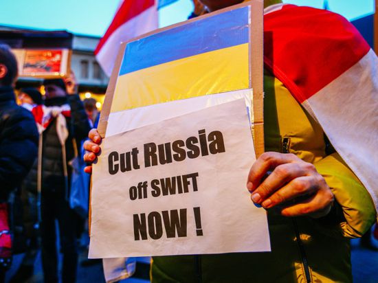Ein Demonstrant hält ein Schild mit der ukrainischen Flagge und der Aufschrift „Russland jetzt abschneiden!“.