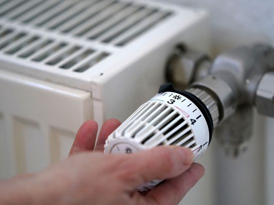 Eine Hand dreht am Thermostat eines Heizkörpers.