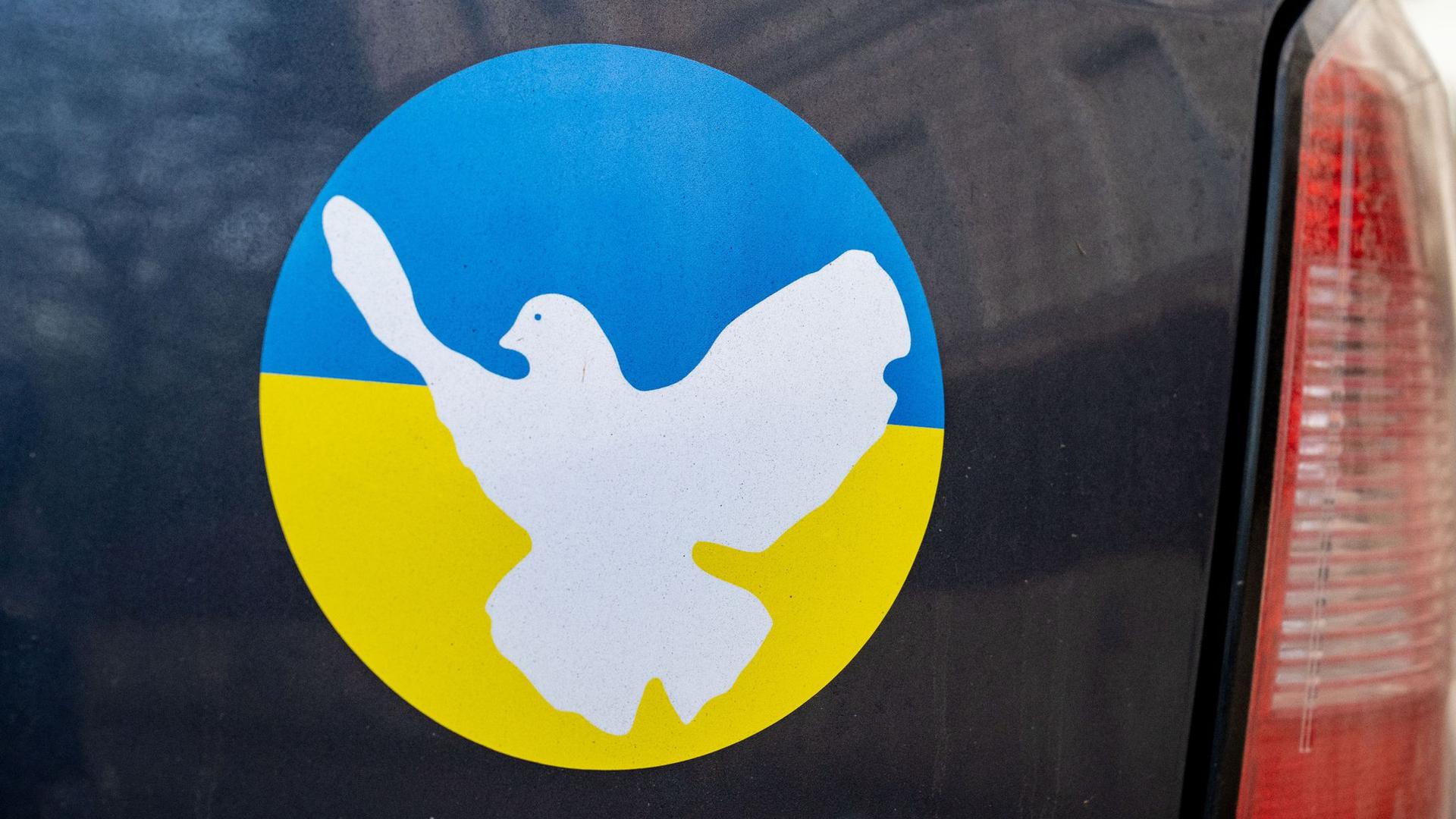 Ein Aufkleber in den Farben der Ukraine und Friedenstauben Symbol auf einer Heckklappe eines Autos.