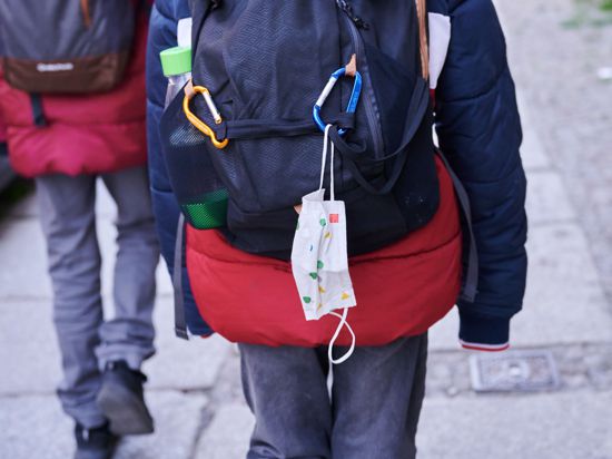 Eine Kindermaske hängt an einem Rucksack eines Schulkindes. Ab Montag fällt die Maskenpflicht in allen Jahrgängen weg.