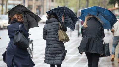 Eine Sturmböe erfasst die Regenschirme von drei Frauen in Frankfurt.