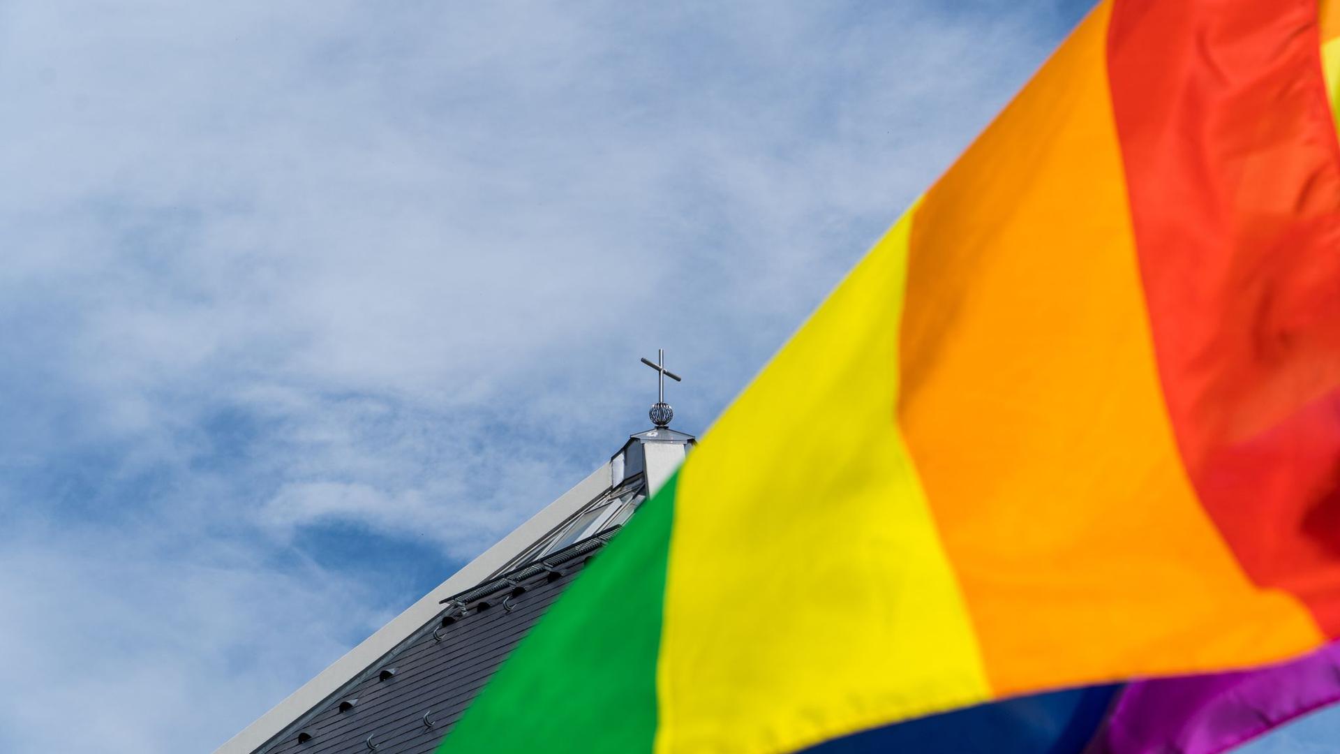 Eine Regenbogenfahne weht vor einer Kirche.