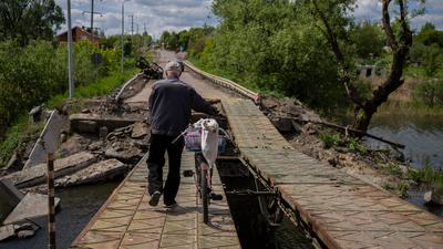 Ein Mann schiebt sein Fahrrad über eine reparierte Brücke im Dorf Wilchiwka am Rande von Charkiw in der Ostukraine.