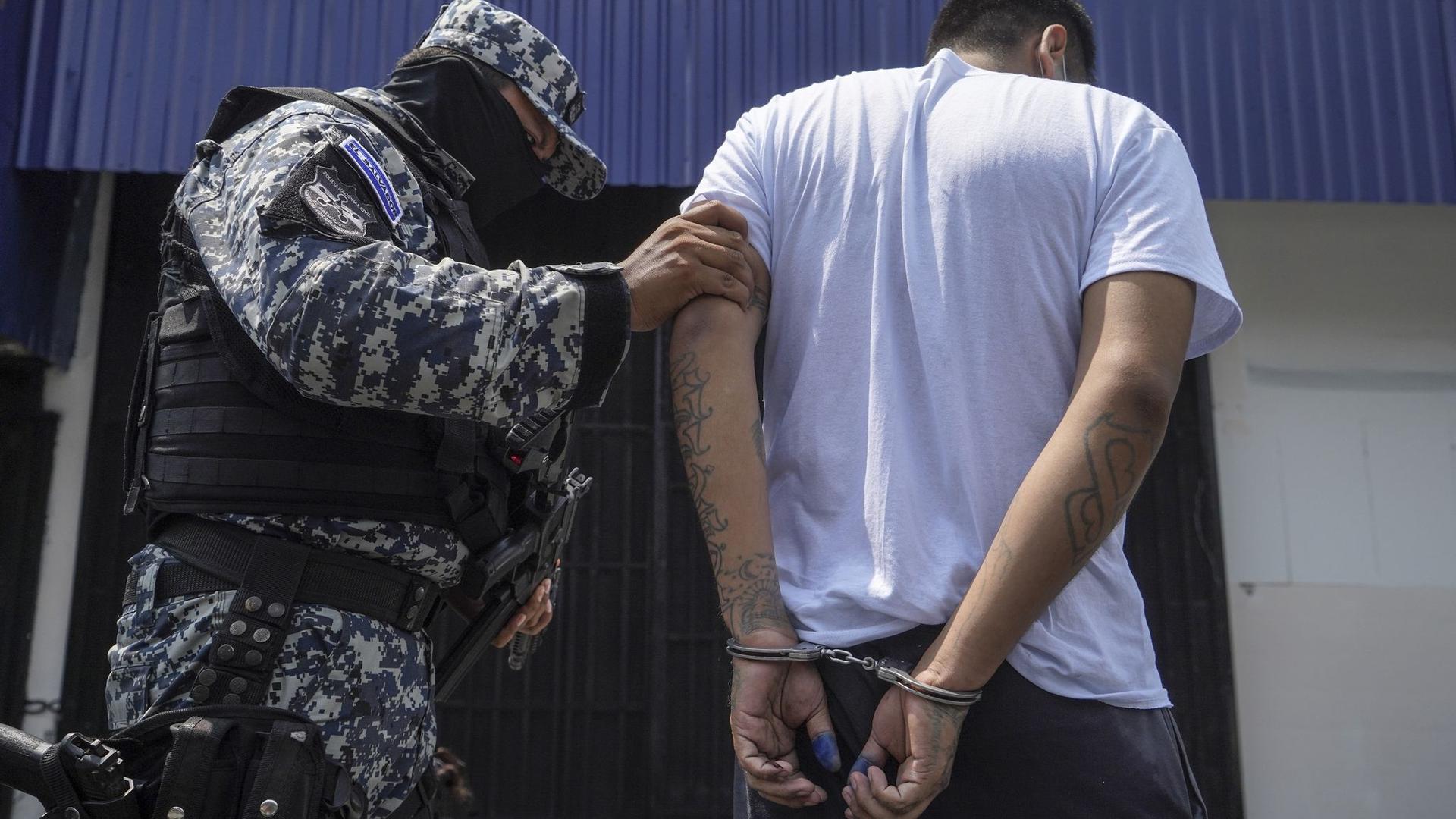 Ein vermummter Polizist in begleitet einen mutmaßlichen Mitglied einer Bande nach dessen Festnahme in San Salvador.