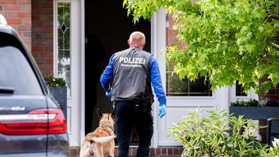 Ein Diensthundeführer der Polizei geht mit einem Spürhund zu einem Wohnhaus in Wiesmoor. Es geht um den Verdacht des Betrugs bei Corona-Hilfen.
