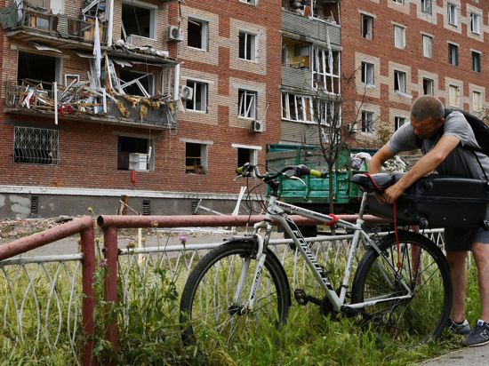 Ein Mann in Slowjansk zurrt einen Koffer auf seinem Fahrrad fest. Das Wohnhaus hinter ihm wurde bei einem nächtlichen Raketeneinschlag beschädigt.