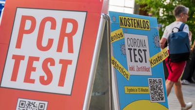 Schilder mit der Aufschrift „PCR Test“ und „Corona-Test – Kostenlos“ hängen vor dem Eingang einer Apotheke in der Innenstadt von München.
