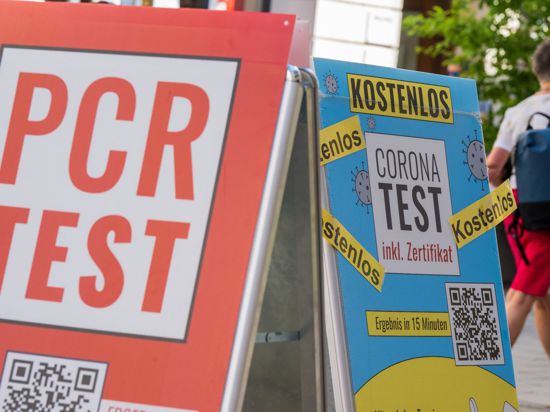 Schilder mit der Aufschrift „PCR Test“ und „Corona-Test – Kostenlos“ hängen vor dem Eingang einer Apotheke in der Innenstadt von München.