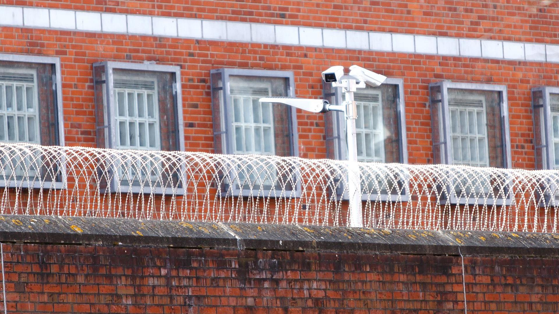 Eine Überwachungskamera steht hinter einem Stacheldrahtzaun der Justizvollzugsanstalt Neumünster.