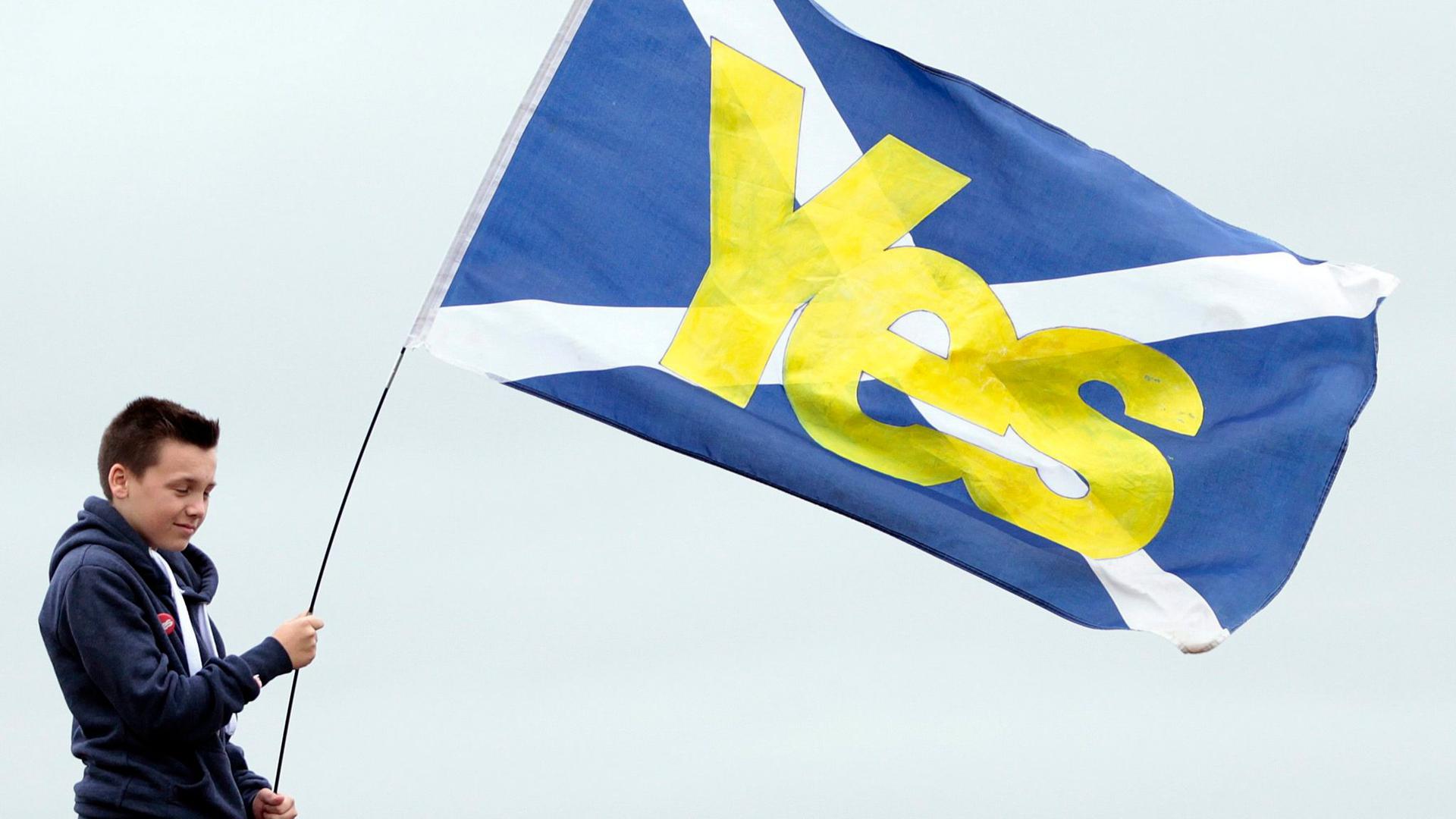 Ein Junge hält eine schottische Flagge mit der Aufschrift „Yes“ in den Händen.