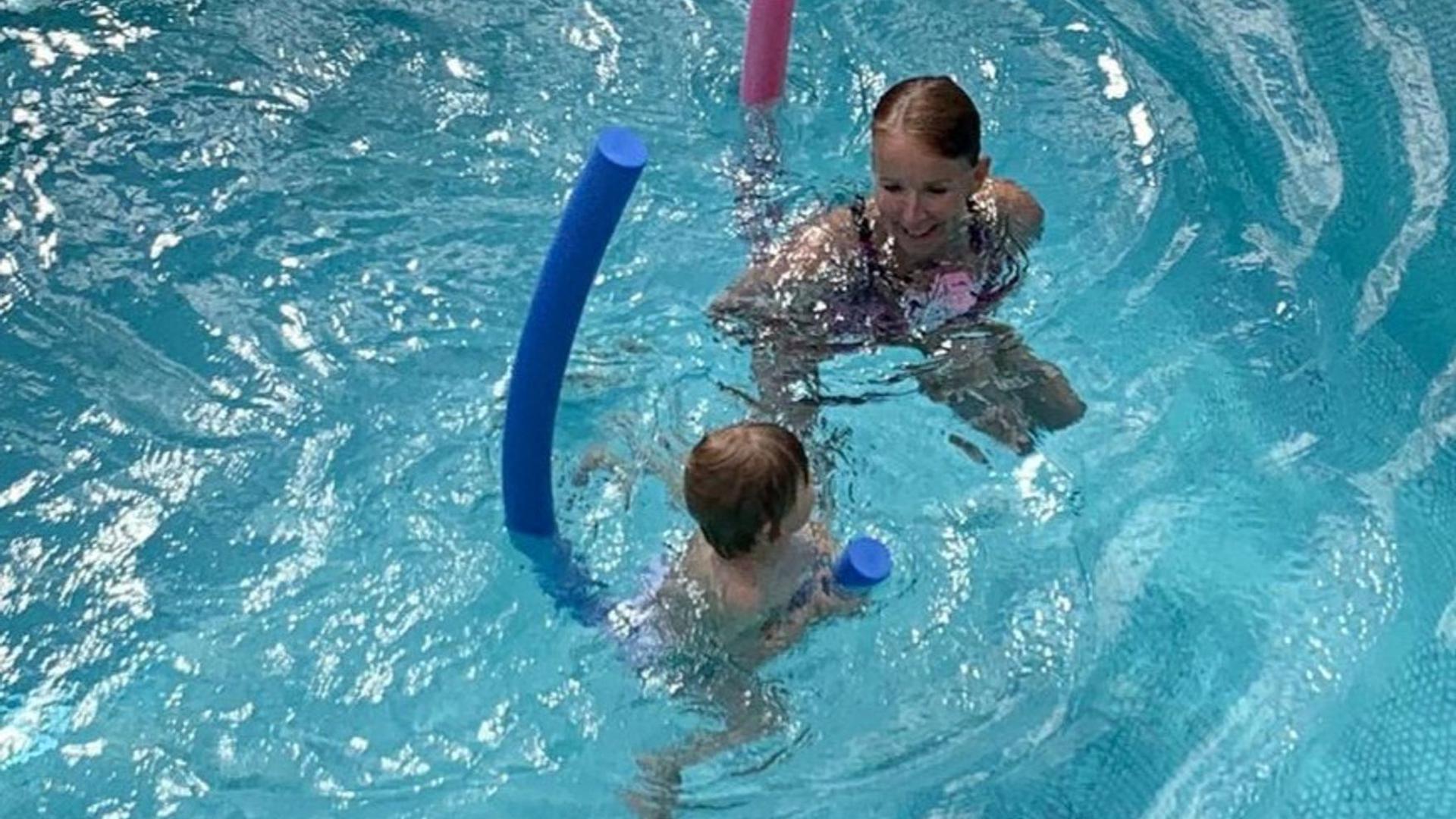 Eine Trainerin übt mit einem Keinkind in einem Becken Schwimmen.