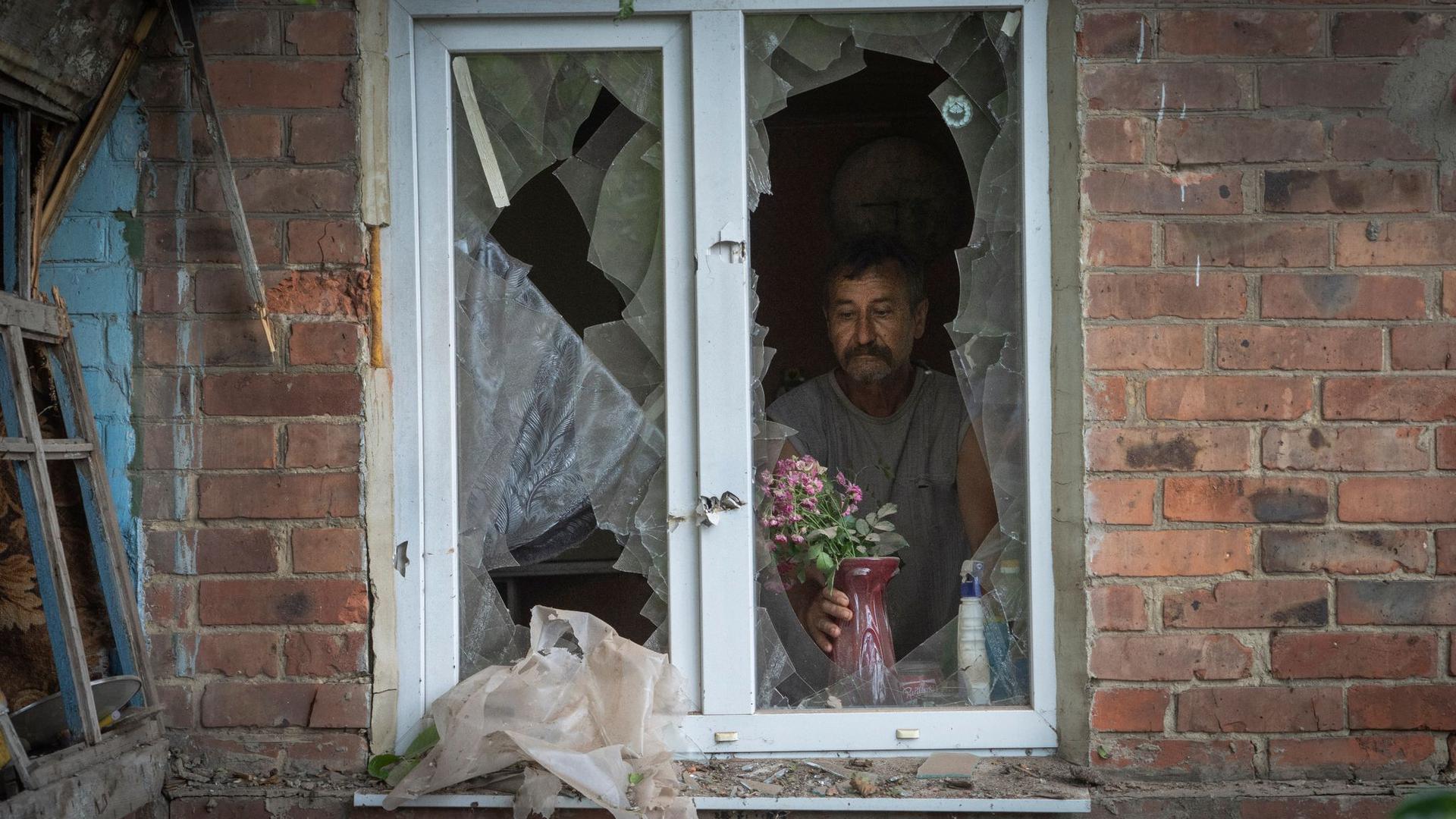Ein Mann in Bachmut stellt in seinem durch russischen Beschuss beschädigten Haus Blumen  auf die Fensterbank.