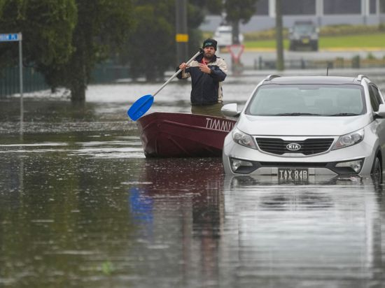 Ein Mann paddelt mit seinem Boot auf einer überfluteten Straße am Stadtrand von Sydney.