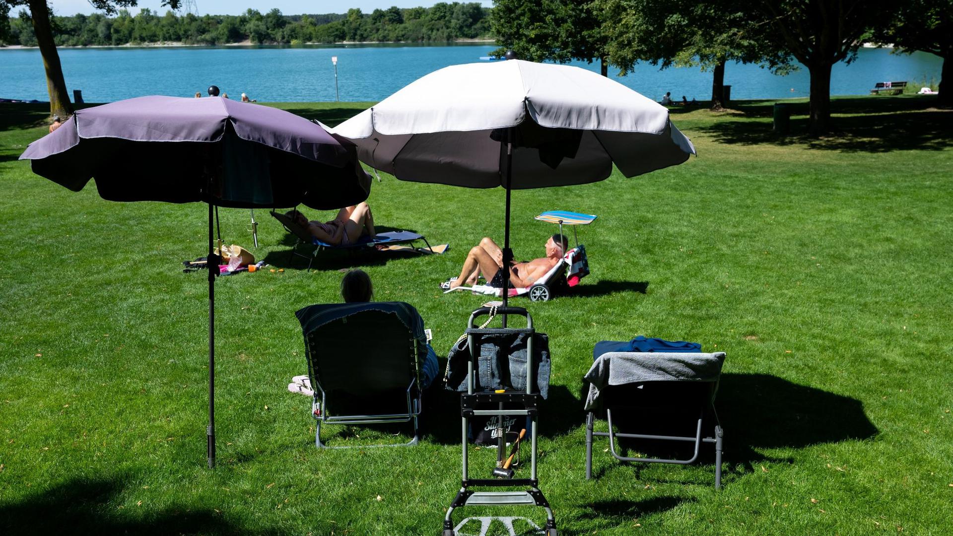 Ausflügler genießen das hochsommerliche Wetter unter Sonnenschirmen am Echinger See.
