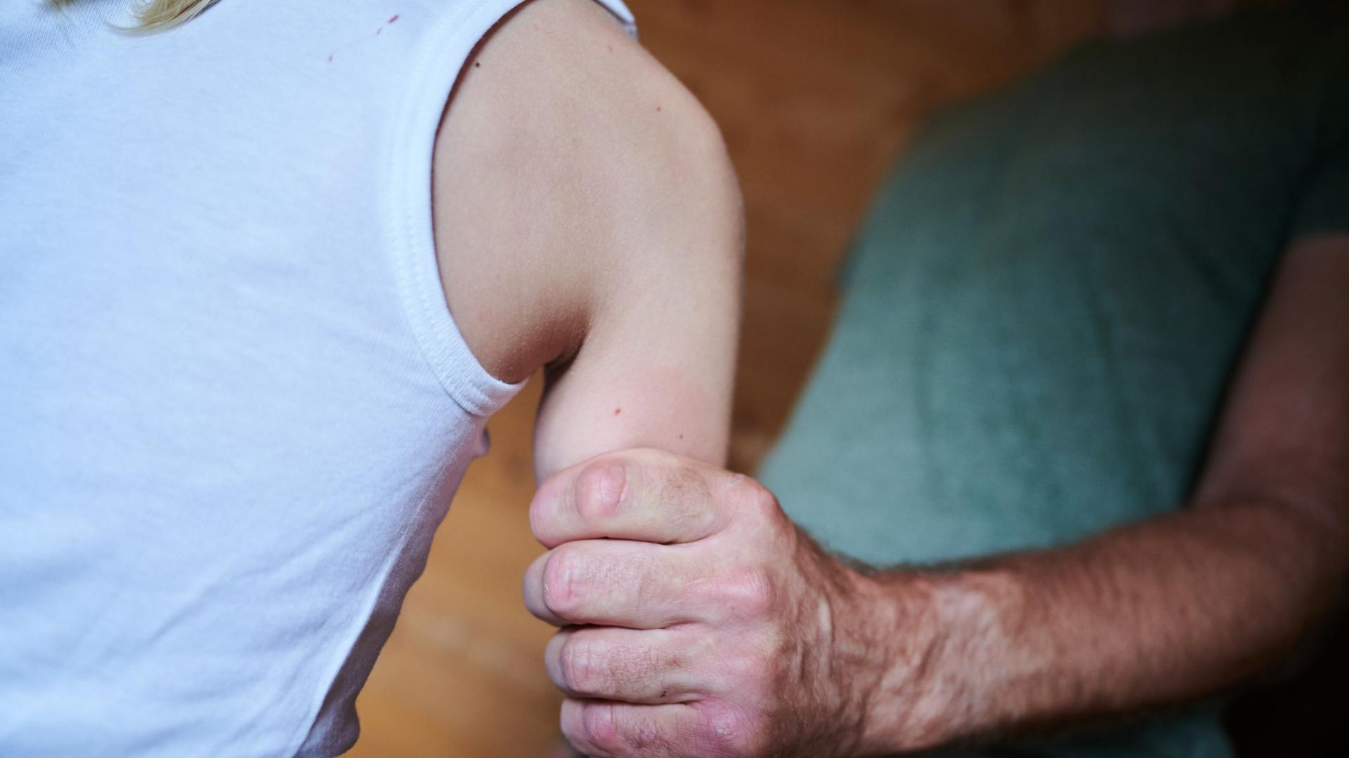 Eine Männerhand umgreift kräftig den nackten Arm eines Kindes