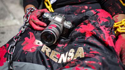 Eine Journalistin und Aktivistin mit einer rot verschmierten Kamera und einer Presseweste bei einer symbolischen Aktion in Mexiko-Stadt.