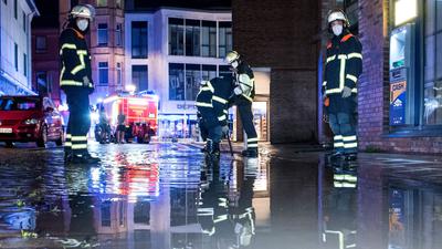Feuerwehrleute pumpen in Hamburg Wasser von einer überfluteten Straße ab.