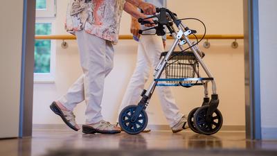 Eine Pflegekraft geht in einem Stuttgarter Pflegeheim mit einer älteren Frau über den Flur.