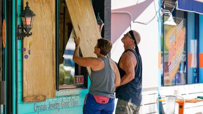 Lisa Bromfield und Mike Sernett bringen eine Sperrholzplatte an den Schaufenstern ihres Geschäfts im US-Bundesstaat Florida an, um sich auf die Ankunft von Hurrikan Ian vorzubereiten.