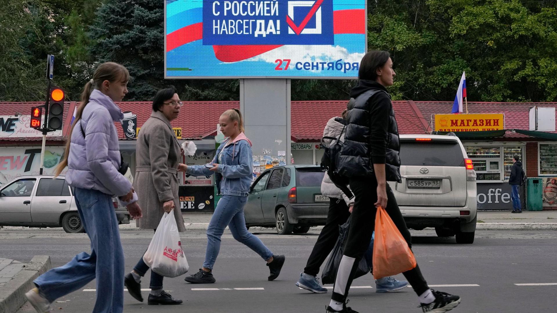 Menschen gehen an einer Anzeige mit der Aufschrift „Für immer mit Russland“ in Luhansk vorbei.