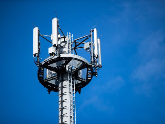 Ein Mast mit verschiedenen Antennen von Mobilfunkanbietern vor blauem Himmel.